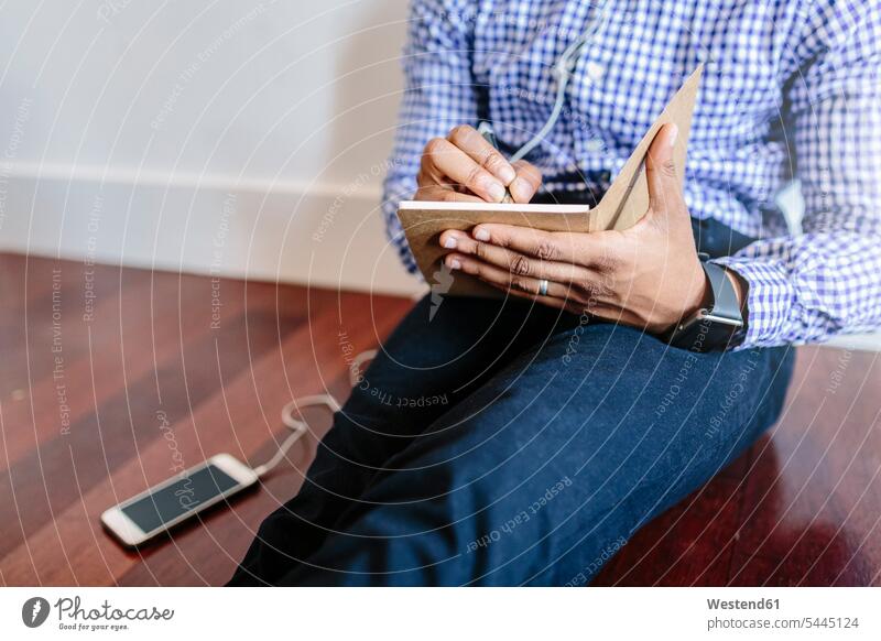 Mann sitzt auf dem Holzboden und schreibt eine Notiz sitzen sitzend Männer männlich Handy Mobiltelefon Handies Handys Mobiltelefone Geschäftsmann Businessmann