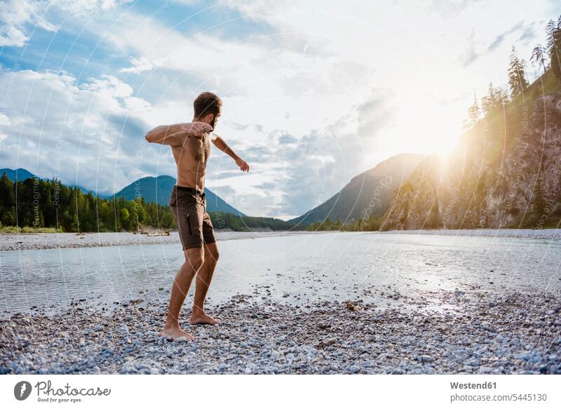 Deutschland, Bayern, am Flussufer stehender Mann beim Steinewerfen Männer männlich Wurf Erwachsener erwachsen Mensch Menschen Leute People Personen Trekking