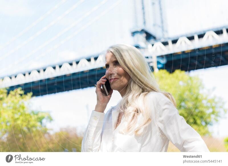 USA, Brooklyn, reife Frau am Telefon vor der Manhattan Bridge weiblich Frauen telefonieren anrufen Anruf telephonieren Smartphone iPhone Smartphones Erwachsener
