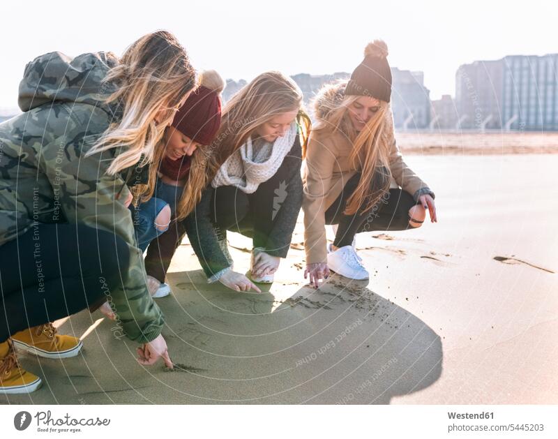 Vier Freunde zeichnen im Sand am Strand Freundinnen Beach Straende Strände Beaches Freundschaft Kameradschaft sandig hocken kauernd hockend ritzen kratzen