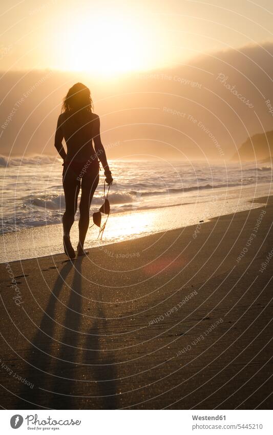 Mexiko, Riviera Nayarit, Silhouette einer Frau, die am Strand in den Sonnenuntergang geht, während sie ihr Bikinioberteil hält Sonnenuntergänge weiblich Frauen