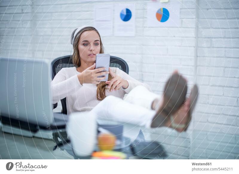 Junge Frau, die im Büro arbeitet und Textnachrichten liest Büroangestellte junge Frau junge Frauen Smartphone iPhone Smartphones SMS sitzen sitzend sitzt lesen
