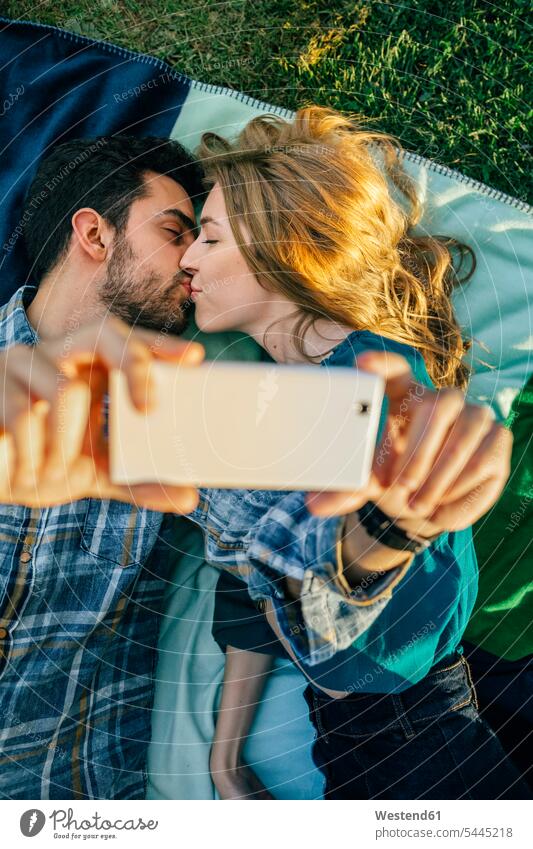 Verliebtes Paar macht Selfie mit Smartphone beim Küssen küssen Kuss Selfies Wiese Wiesen fotografieren Pärchen Paare Partnerschaft liegen liegend liegt iPhone