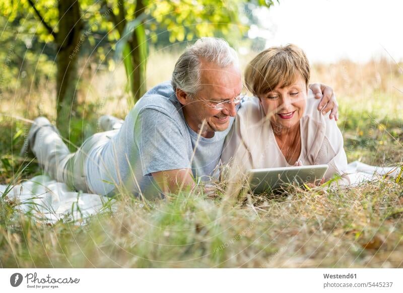 Glückliches älteres Ehepaar mit Tablette auf der Wiese liegend lächeln Tablet Computer Tablet-PC Tablet PC iPad Tablet-Computer liegt Paar Pärchen Paare