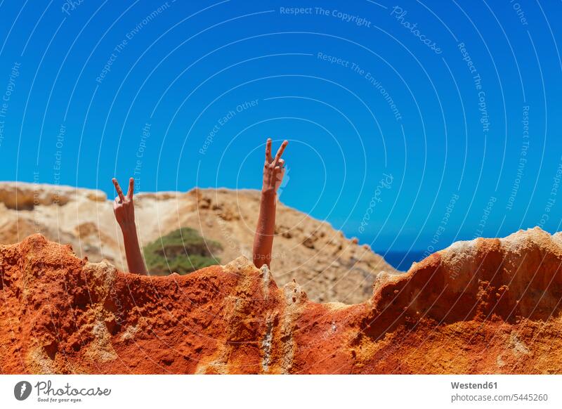 Frau macht Siegeszeichen hinter Felsen am Strand Himmel Reise Travel Freizeit Muße versteckt Quality Time Portugal Humor humorvoll lustig spaßig Lebensqualität