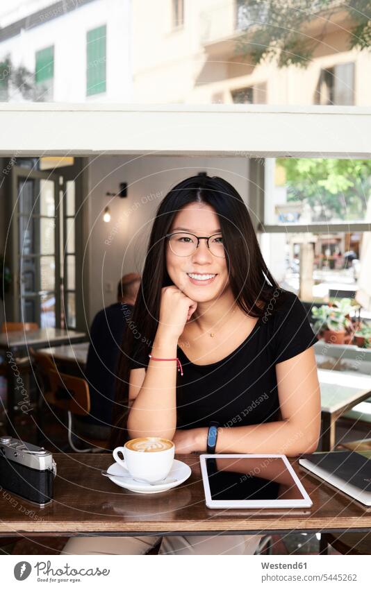 Porträt einer asiatischen jungen Frau, die in einem Café in die Kamera lächelt Zufriedenheit zufrieden Touristin sitzen sitzend sitzt weiblich Frauen Asiatin