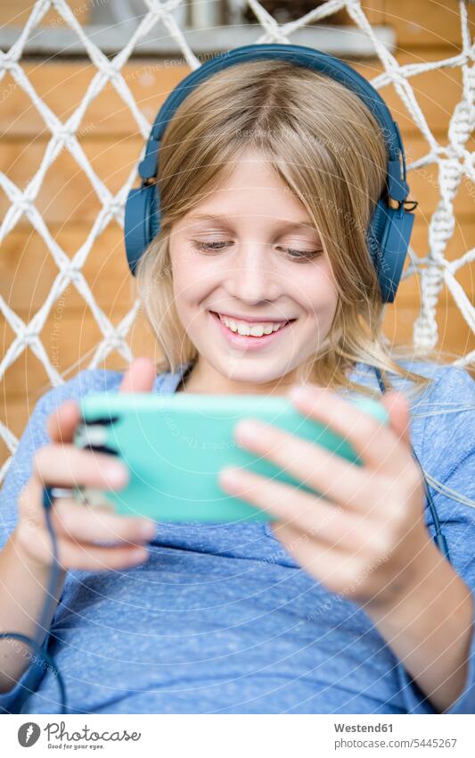 Porträt eines glücklichen Mädchens mit Kopfhörer und Smartphone in einem Hängesessel Kopfhoerer weiblich Glück glücklich sein glücklichsein iPhone Smartphones