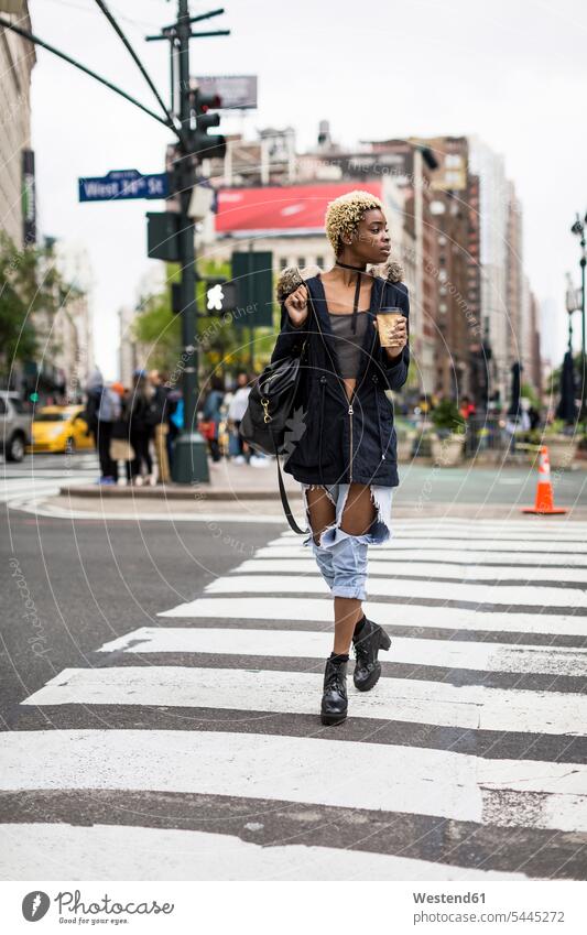 USA, New York City, modische junge Frau mit Kaffee zum Überqueren der Straße überqueren Strassen Straßen Coffee to go zum mitnehmen weiblich Frauen gehen gehend