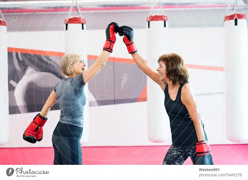 Zwei glückliche ältere Frauen mit Boxhandschuhen im Fitnessstudio Senioren alte Frauenboxen Spaß Spass Späße spassig Spässe spaßig Training trainieren