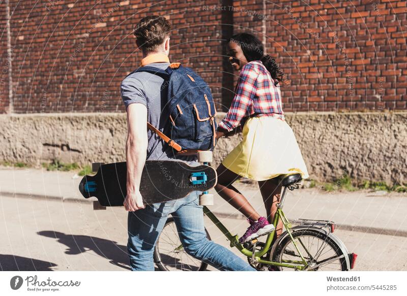 Junges Paar mit Fahrrad und Skateboard auf der Straße multikulturell gehen gehend geht Rollbretter Skateboards Pärchen Paare Partnerschaft jung Strassen Straßen