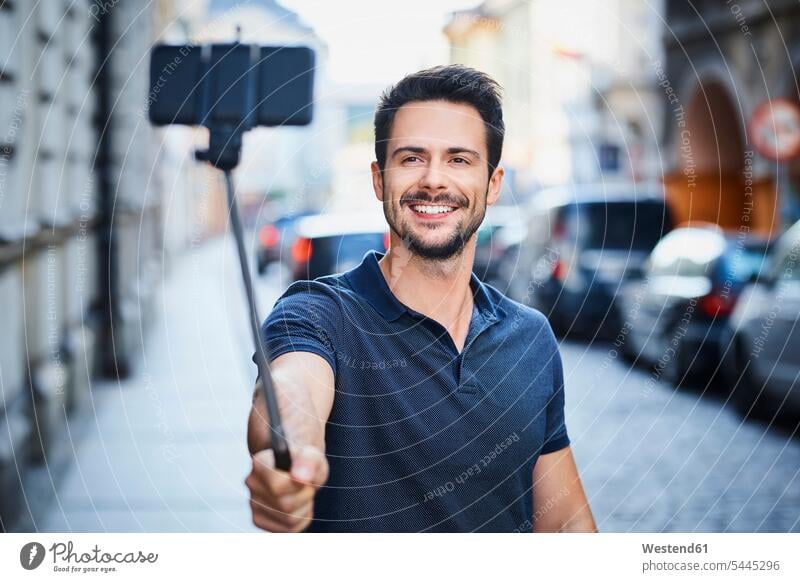 Mann, der ein Foto mit einem Smartphone auf einem Selfie-Stick macht Männer männlich glücklich Glück glücklich sein glücklichsein Selfies lächeln Handy