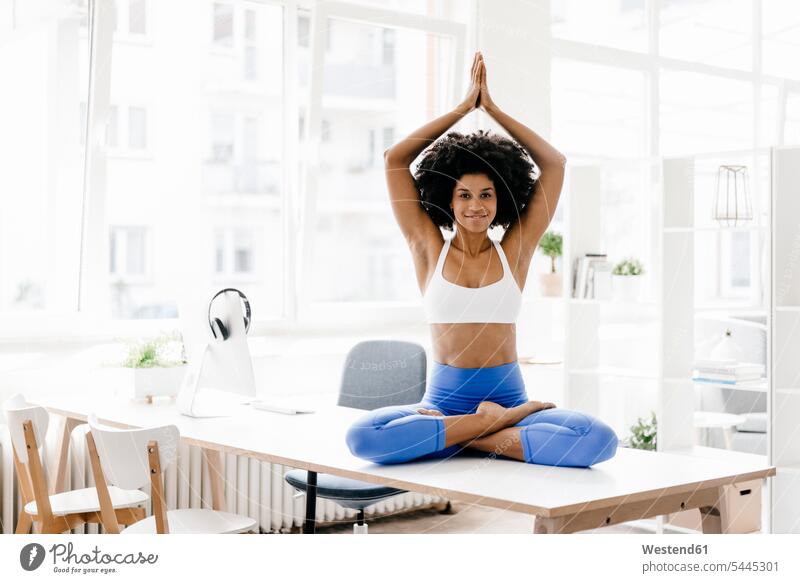 Junge Frau praktiziert Yoga auf ihrem Schreibtisch sitzen sitzend sitzt Lotussitz Lotusposition Lotuspositionen Schneidersitz fit meditieren Training trainieren