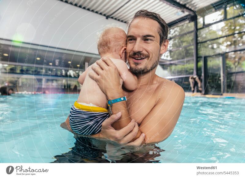 Vater hält Baby in der Schwimmhalle Hallenbad Hallenbäder Hallenbaeder Papas Väter Vati Vatis Papis lächeln Schwimmbad Schwimmbaeder Schwimmbäder Babies Babys