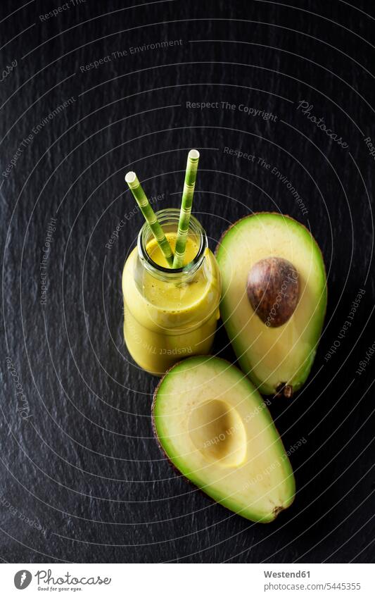Glasflasche mit Avocado-Smoothie und geschnittener Avocado auf Schiefer Draufsicht Vogelperspektive von oben Aufsicht Avocados Persea americana Hälfte halbe