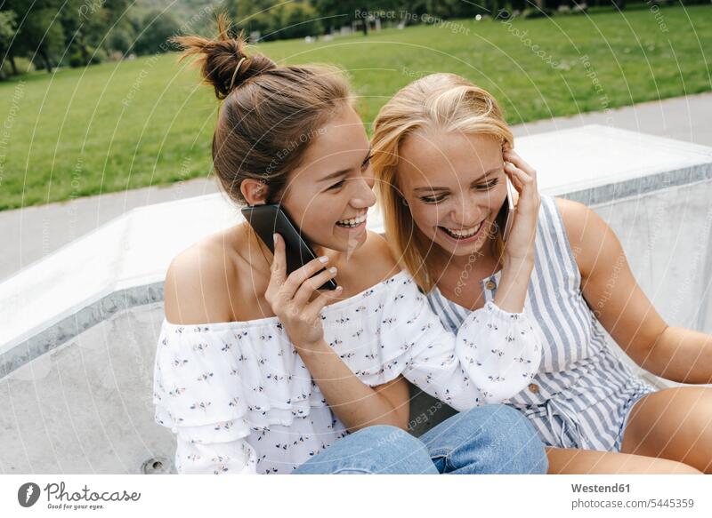 Zwei glückliche junge Frauen mit Mobiltelefonen in einem Skatepark Freundinnen weiblich Glück glücklich sein glücklichsein Park Parkanlagen Parks Skateboardpark