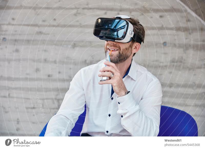 Auf Stuhl sitzender Mann mit VR-Brille sitzt lächeln Geschäftsmann Businessmann Businessmänner Geschäftsmänner Männer männlich Virtual Reality Brille