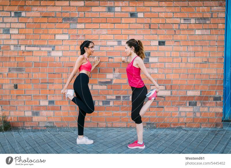 Zwei aktive Frauen strecken sich an einer Ziegelmauer Freundinnen dehnen Trainieren Übung Üben Übungen Backsteinwand Backsteinmauern weiblich Freunde