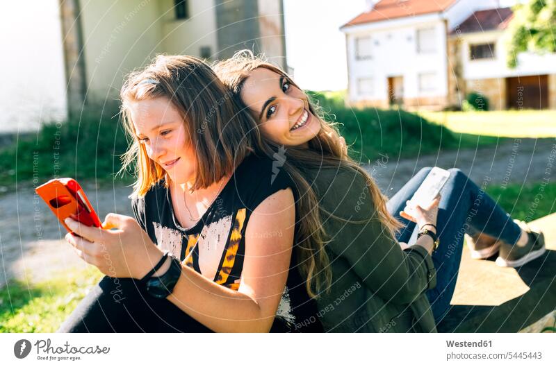 Zwei glückliche Mädchen benutzen ihre Smartphones im Freien Glück glücklich sein glücklichsein weiblich Schwester Schwestern Handy Mobiltelefon Handies Handys