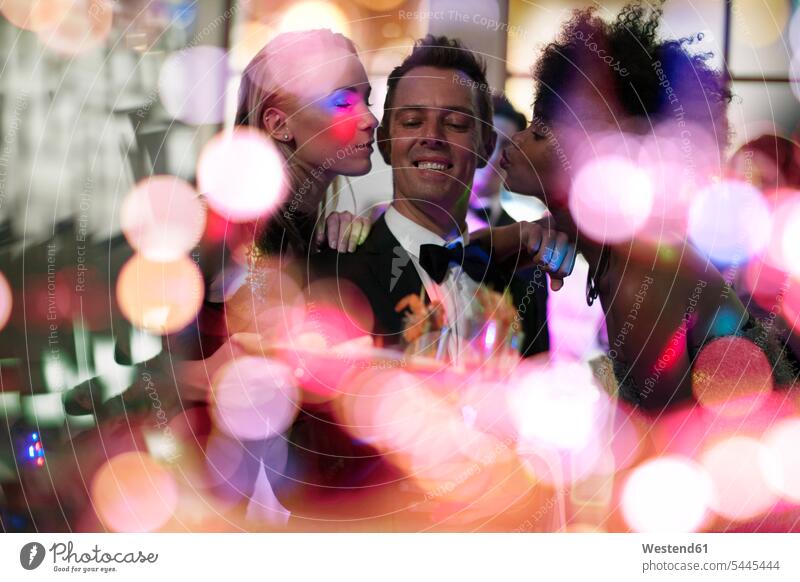 Zwei Frauen küssen Mann im Smoking auf einer Party Parties Partys Kellner Ober feiern Feier Fest Festlichkeit Feiern Festlichkeiten Feste Bedienung