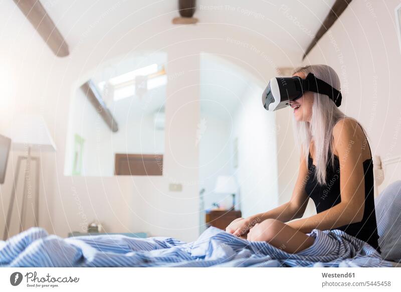 Junge Frau sitzt im Bett und trägt eine VR-Brille Brillen Virtuelle Realität Virtuelle Realitaet Betten weiblich Frauen sitzen sitzend Erwachsener erwachsen