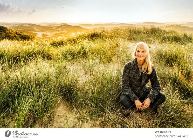 Porträt einer lächelnden Frau, die in den Dünen sitzt Strand Beach Straende Strände Beaches weiblich Frauen Sanddüne Sanddünen sitzen sitzend Erwachsener