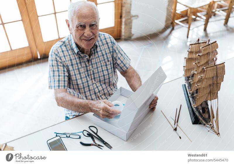 Porträt eines selbstbewussten älteren Mannes, der ein Paket auspackt, mit einem Schiffsmodell auf dem Tisch auspacken lächeln Männer männlich Senior