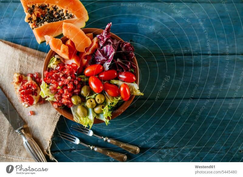 Papayasalat, Granatapfel, Kopfsalat, Tomate, Oliven und Endivie auf blauem Holz Vitamine Granatapfelkerne Kern Kerne Speisetomaten Tomaten Gesunde Ernährung