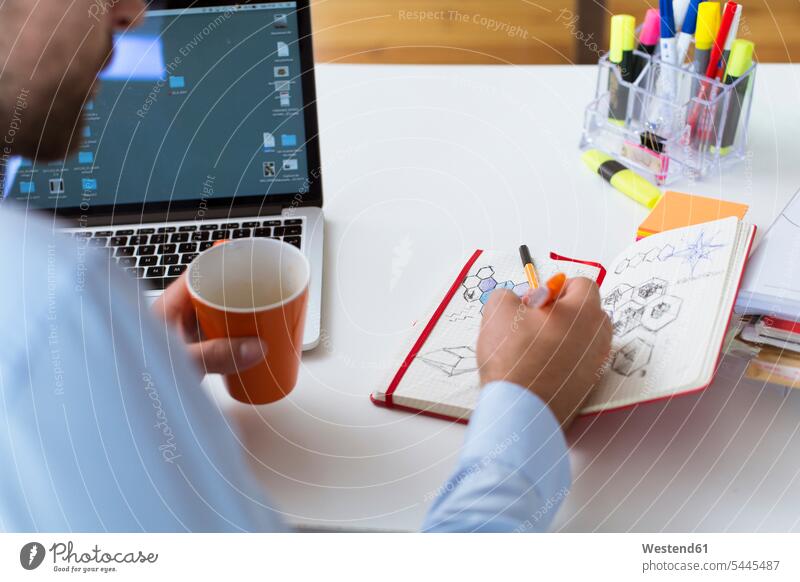Mann zieht am Schreibtisch im Büro in ein Notizbuch Arbeitstisch Schreibtische Notizbücher Notizbuecher zeichnen Zeichnung Office Büros Tisch Tische