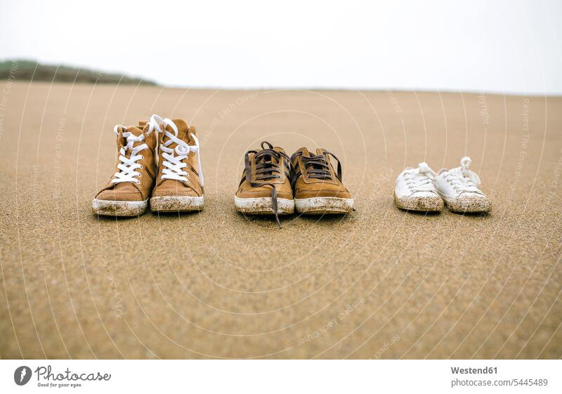 Drei Paar Schuhe in verschiedenen Größen am Strand Sand sandig Beach Straende Strände Beaches Größenunterschied Nahaufnahme Nahaufnahmen Großaufnahme close up