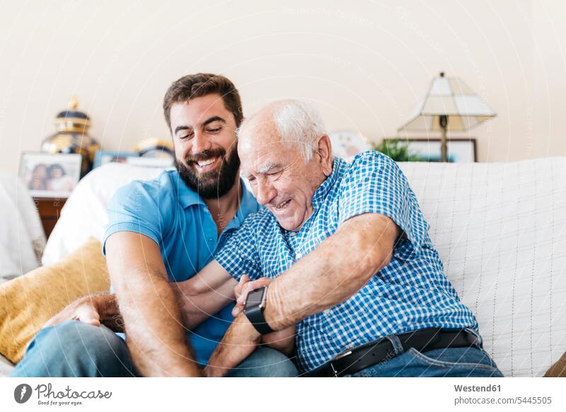 Der erwachsene Enkel und sein Großvater sitzen zu Hause auf der Couch und kitzeln sich gegenseitig Enkelsöhne Enkelsohn Opa Großpapa Großpapas Opas Opi