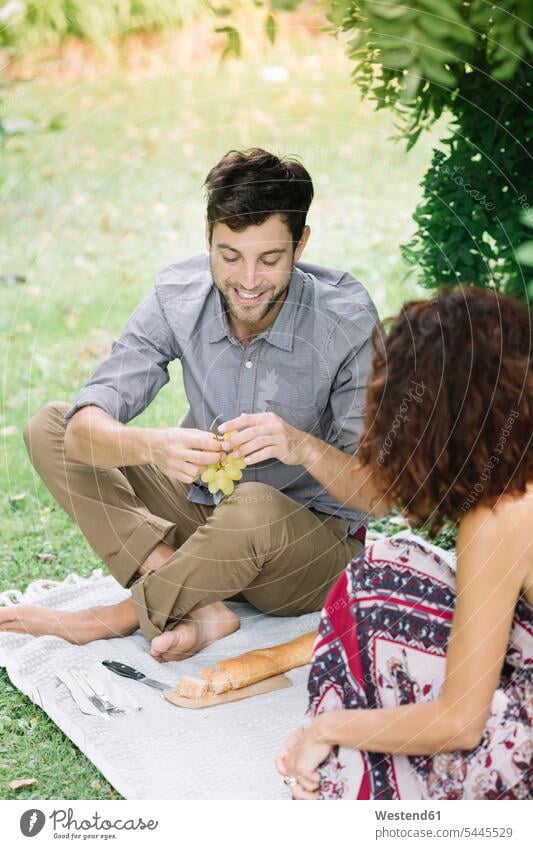 Glückliches Paar beim Picknick im Park Pärchen Paare Partnerschaft picknicken Parkanlagen Parks lächeln Mensch Menschen Leute People Personen Mahlzeit
