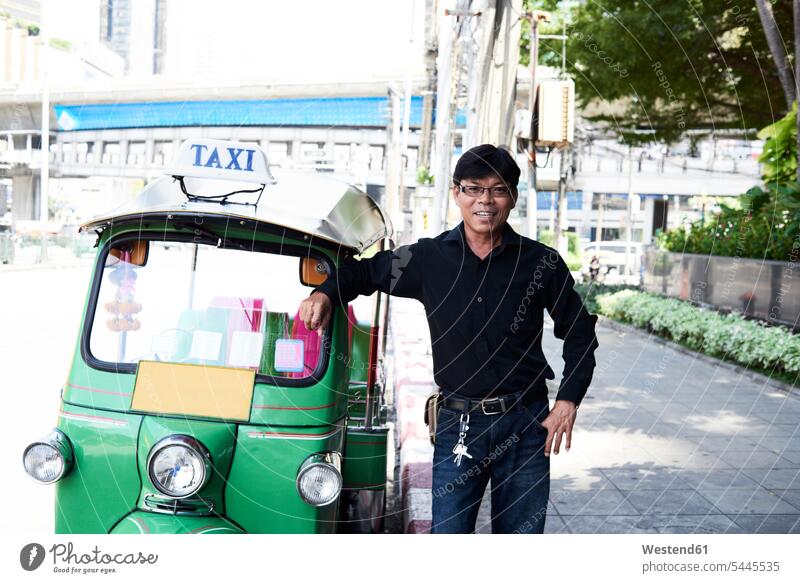 Thailand, Bangkok, Tuk-Tuk-Fahrer steht neben seinem Fahrzeug auf der Straße Städtische Straße Strassen Straßen Dreiviertelansicht Schrift Text Brille Brillen