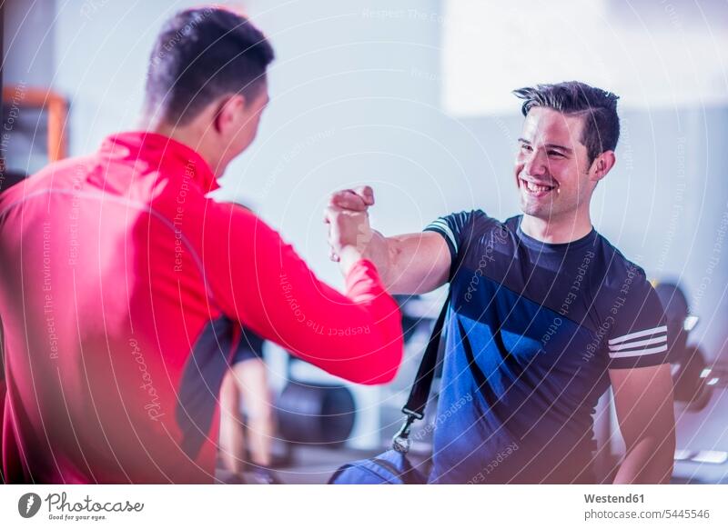 Zwei junge Männer schütteln sich in der Turnhalle die Hand lächeln trainieren Freunde Fitnessstudio Fitnessclubs Fitnessstudios Freundschaft Kameradschaft fit
