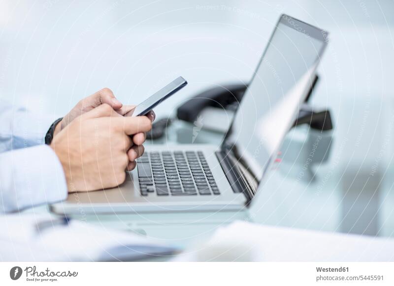 Geschäftsmann mit Smartphone am Schreibtisch mit Laptop Business Geschäftsleben Geschäftswelt geschäftlich arbeiten Arbeit Beruf Berufstätigkeit Berufe