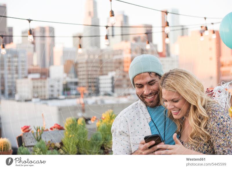 Junges Paar mit Luftballons steht auf der Dachterrasse und benutzt ein Smartphone glücklich Glück glücklich sein glücklichsein iPhone Smartphones betrachten