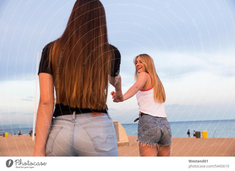 Zwei glückliche junge Frauen Hand in Hand am Strand Beach Straende Strände Beaches Freundinnen weiblich Freunde Freundschaft Kameradschaft Erwachsener erwachsen
