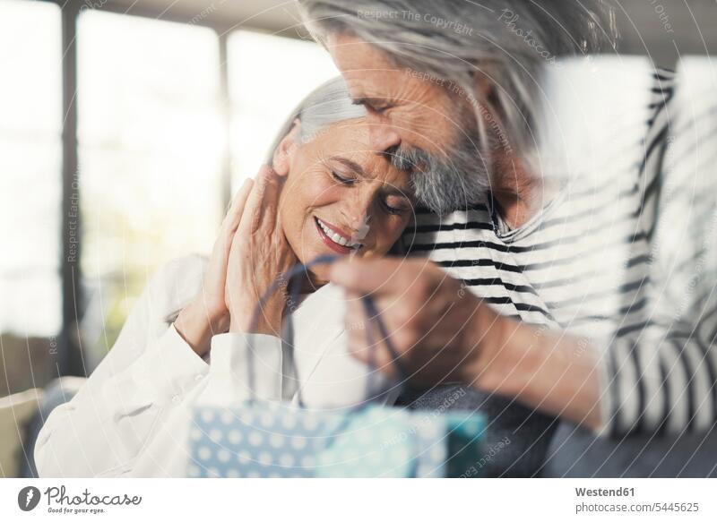 Älterer Mann überrascht Ehefrau mit einem Geschenk Senioren alte ältere schenken Überraschung überraschen Paar Pärchen Paare Partnerschaft lächeln Freude freuen