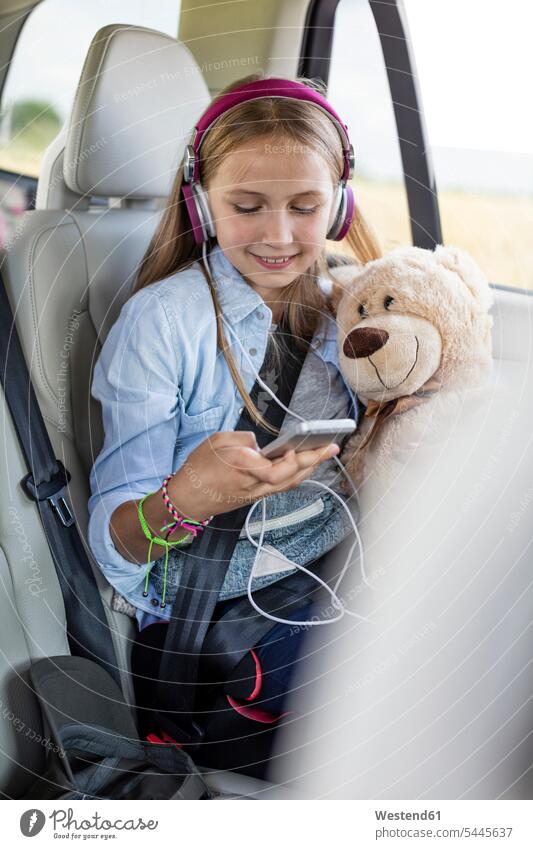 Mädchen sitzt im Auto, hält Teddybär und hört Musik weiblich Autoreise Urlaub Ferien sitzen sitzend lächeln hören hoeren halten Wagen PKWs Automobil Autos