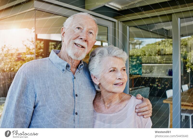 Älteres Ehepaar steht vor ihrem Haus und sieht selbstbewusst aus Ehepaare glücklich Glück glücklich sein glücklichsein stehen stehend Terrasse Terrassen