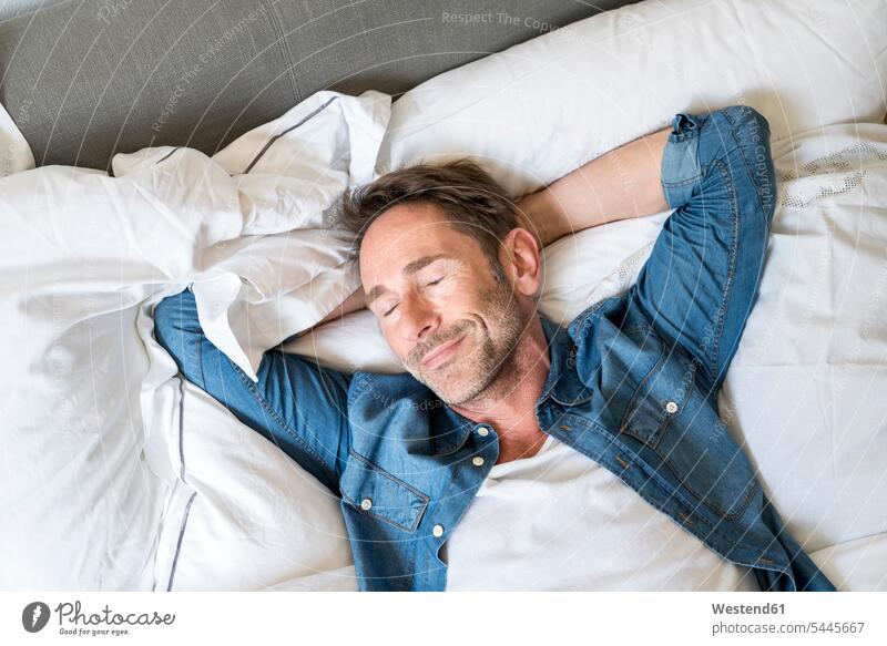 Bildnis eines reifen Mannes auf dem Bett liegend mit geschlossenen Augen und Händen hinter dem Kopf Betten Männer männlich Portrait Porträts Portraits