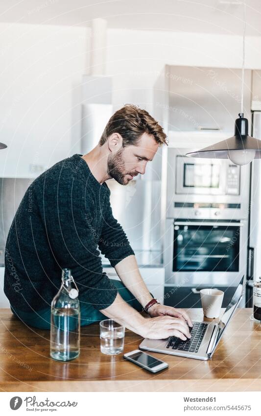 Mann sitzt in der Küche mit Laptop auf der Arbeitsplatte Männer männlich Notebook Laptops Notebooks Erwachsener erwachsen Mensch Menschen Leute People Personen