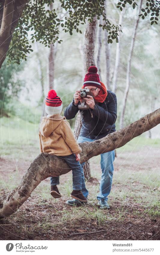 Vater macht ein Foto von seinem Sohn, wie er auf einem Baumstamm im Wald sitzt fotografieren Junge Buben Knabe Jungen Knaben männlich Papas Väter Vati Vatis
