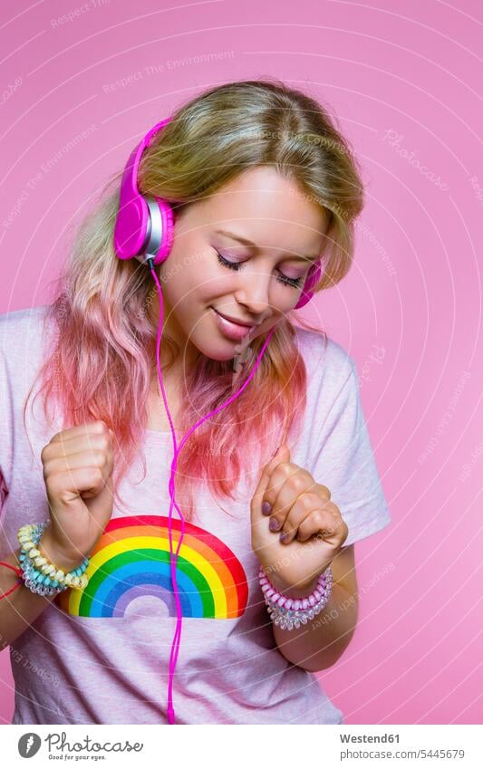 Porträt einer tanzenden jungen Frau, die mit Kopfhörern vor rosa Hintergrund Musik hört weiblich Frauen Kopfhoerer Portrait Porträts Portraits Erwachsener