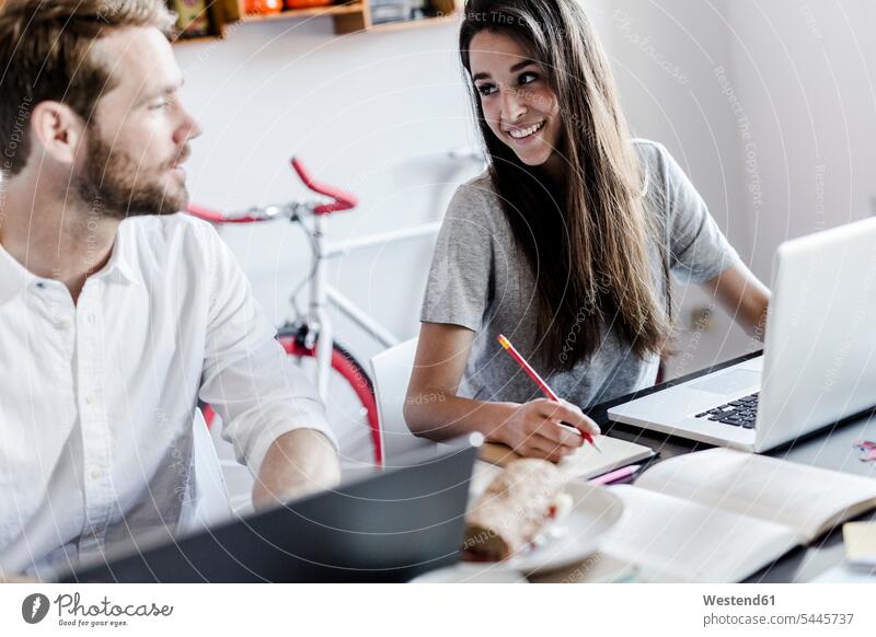 Lächelnde Frau zu Hause, die einen Laptop benutzt und ihren Freund anschaut Notebook Laptops Notebooks Zuhause daheim Paar Pärchen Paare Partnerschaft lächeln