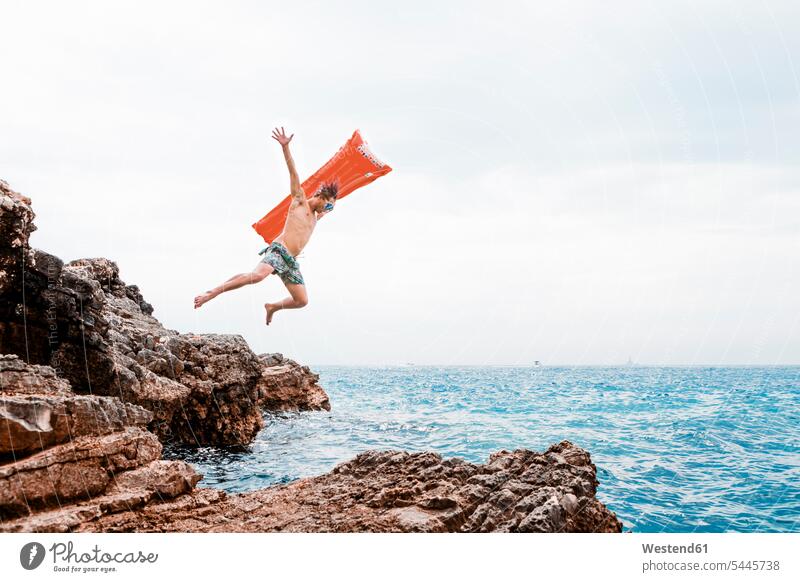 Mann mit Luftmatratze springt von Felsen ins Meer Meere Männer männlich springen hüpfen Gewässer Wasser Erwachsener erwachsen Mensch Menschen Leute People