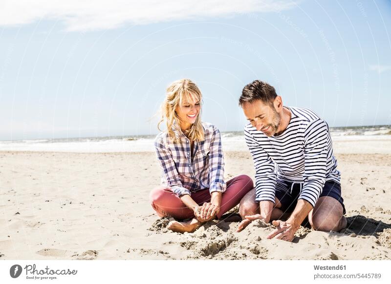 Glückliches Paar sitzt am Strand Pärchen Paare Partnerschaft Sand sandig Beach Straende Strände Beaches lächeln sitzen sitzend Mensch Menschen Leute People