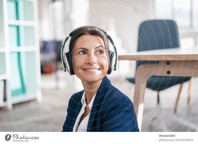 Porträt einer lächelnden Geschäftsfrau in einem Loft, die mit Kopfhörern Musik hört Kopfhoerer Portrait Porträts Portraits Frau weiblich Frauen Erwachsener