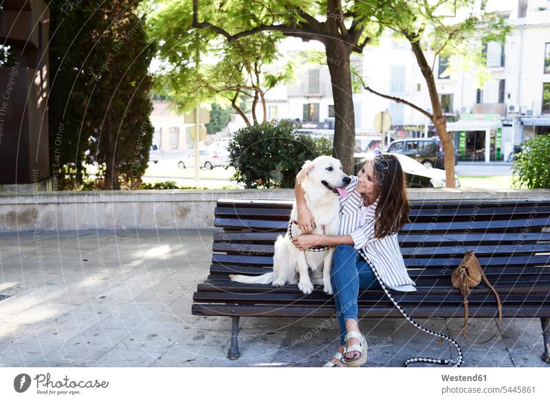 Glückliche junge Frau sitzt mit ihrem Hund auf einer Bank in der Stadt weiblich Frauen glücklich glücklich sein glücklichsein Hunde Sitzbänke Bänke Sitzbank