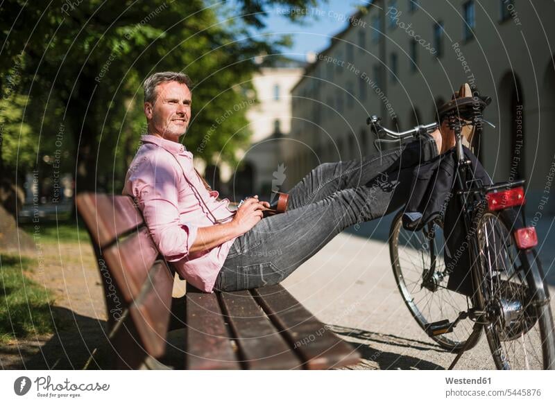 Mann mit Fahrrad und altmodischer Kamera entspannt sich auf einer Parkbank Männer männlich entspanntheit relaxt sitzen sitzend sitzt Fotoapparat Fotokamera