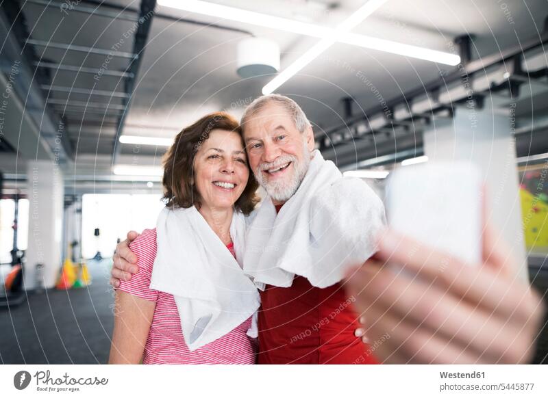 Ein fittes älteres Paar macht Selfies mit dem Smartphone im Fitnessstudio Senioren alte Fitnessclubs Fitnessstudios Turnhalle trainieren Workout Sport aktiv